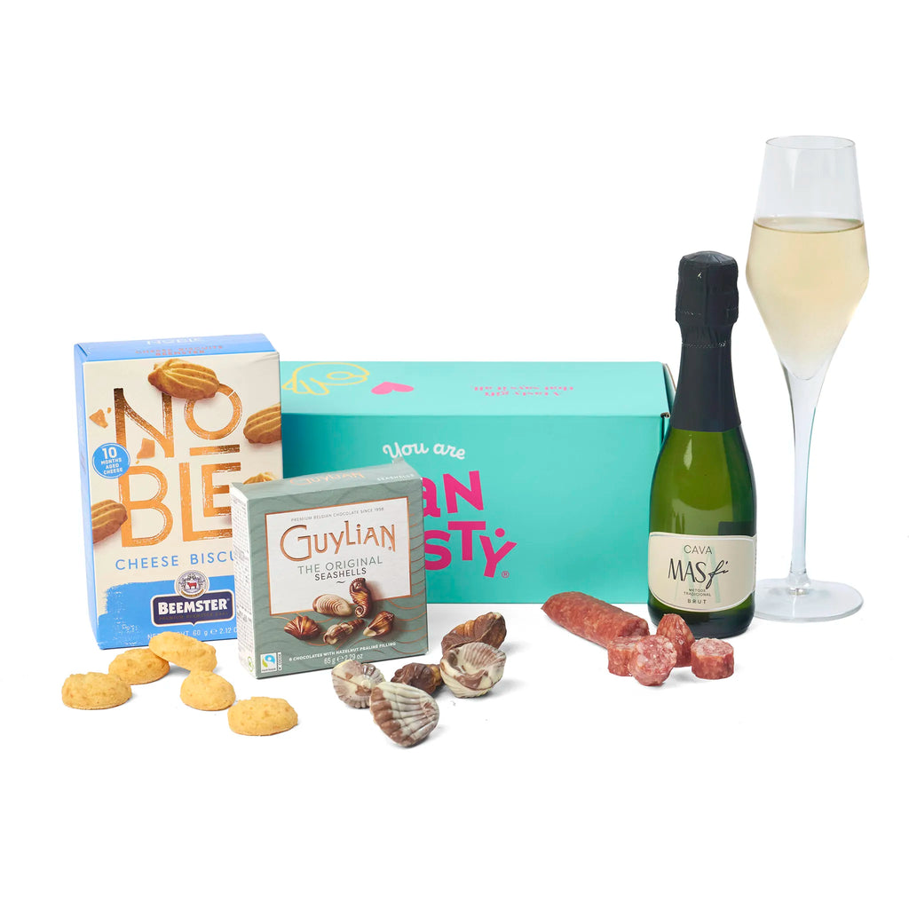 Sfeerbeeld van het Cava Aperitief Geschenk met losse hartige snacks en chocolade naast de doos